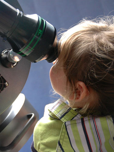 Fetita observa stelele prin telescop