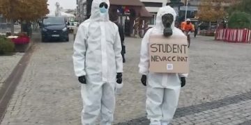 Doi tineri s-au plimbat în combinezoane de protecție cu mesajul: „Student nevaccinat”