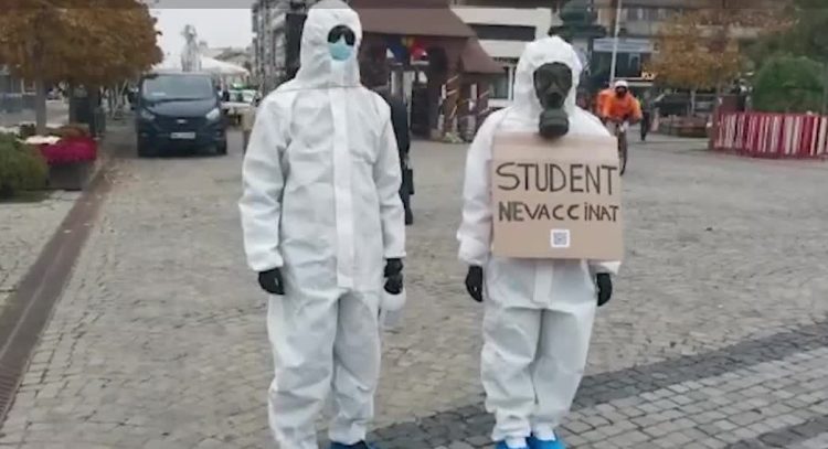 Doi tineri s-au plimbat în combinezoane de protecție cu mesajul: „Student nevaccinat”